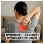 肩甲骨の間に痛みを感じて手を当てる女性の背中の写真
